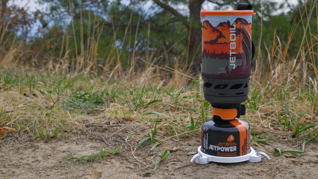 Camping stove stabilizer supporting a Jetboil fuel canister on uneven outdoor ground