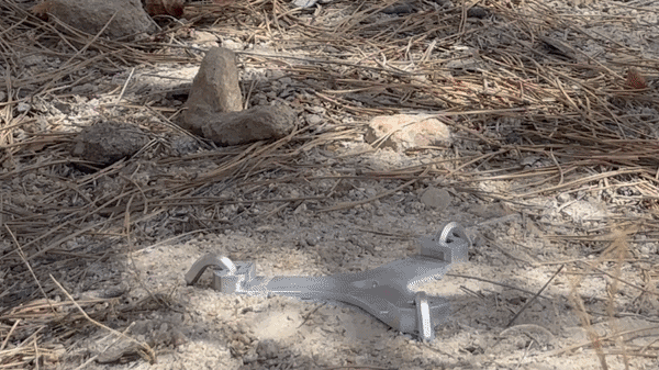 Camping stove stabilizer staked into dirt, showing gas canister interface sliding on vertically for quick setup and removal.